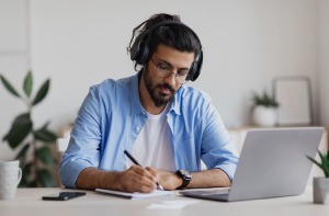 An employee going through a e-learning program while listening to audio and taking notes.